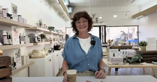 A photo of Jewels Burdick, Founder of Simple Body, standing in the retail store holding a cup of coffee and smiling.