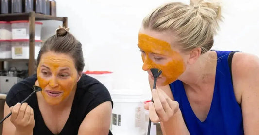 A photo of two young women applying a Simple Body Caramel Clay Face Mask with Fan Brushes in their hands.