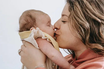 A photo of a mother kissing her newborn and smiling
