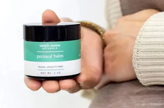 A closeup photo of a pregnant mama holding up a jar of Simple Mama Perineal Balm which has a teal green label and is vegan and cruelty-free.
