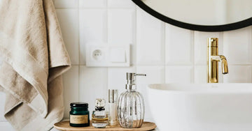 A photo of a beautiful, simple bathroom with minimal skincare products, a beige towel hanging and a gold faucet.