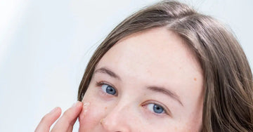 A photo of a young woman with beautiful blue eyes applying Eye Defense Serum by Simple Body