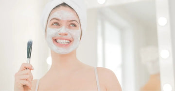 A photo of a young woman smiling with a Simple Body Kaolin Clay Mask on holding a brush.