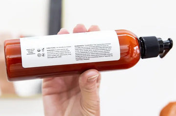 A hand holding up a bottle of Simple Body Lavender Lotion on the side so you can see the label and ingredient deck.