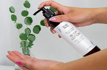 A photo of two youthful hands with fun painted fingernails holding a bottle of Simple Body Body Lotion in Lavender, preparing to put some on her hands.