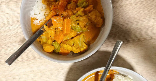 A close up photo of a bowl of curry with carrots, broccoli and other vegetables on top of rice.
