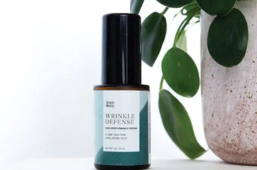 A photo of Simple Body Wrinkle Defense Serum sitting next to a beige ceramic pot and a healthy green plant.