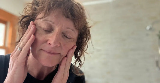 A photo of Jewels, Founder of Simple Body with her eyes closed, massaging her temples as she applies her skincare.