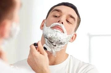 A photo of a young man looking in the mirror with shaving cream on his face shaving