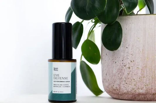 A photo of Simple Body Eye Defense Serum sitting next to a healthy green plant in a beige colored ceramic vessel
