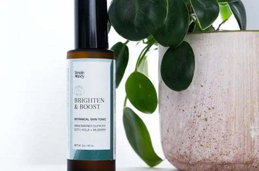 A photo of Simple Body Brighten + Boost Botanical Skin Tonic sitting next to a ceramic beige pot with a green plant in it.