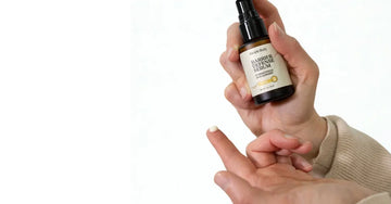 A photo of a hand holding a bottle of Simple Body Barrier Defense Serum. There's a drop of the Barrier Defense Serum on her fingertip showing off the creamy white texture.