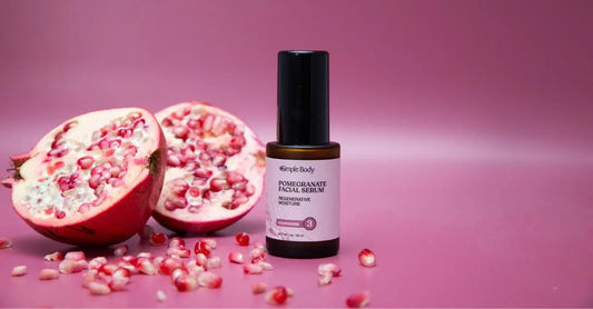 A photo of a pomegranate cut in half with seeds spilling out and a bottle of Simple Body Pomegranate Facial Serum sitting next to it.