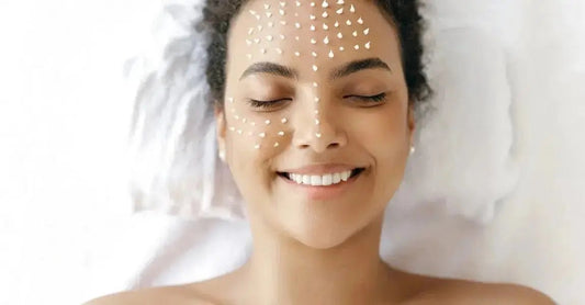 A young woman laying down with her eyes closed, smiling with dots of Simple Body Face Cream on her skin.