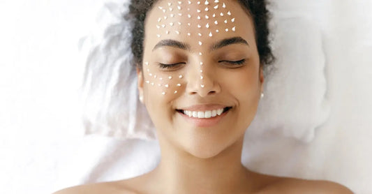 A young woman laying down with her eyes closed, smiling with dots of Simple Body Face Cream on her skin.