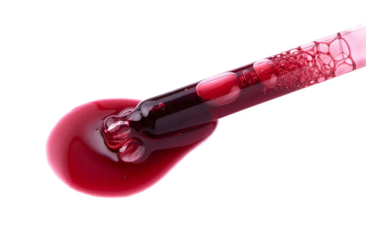 Deep red antioxidant facial serum dripping from glass pipette on white background