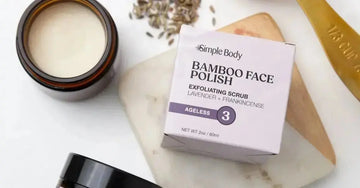 A photo of Simple Body Bamboo Face Polish in Lavender and Frankincense sitting on a marble coaster with one next to it with the top off showing the creamy texture with lavender seeds in the background.