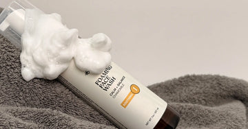 A photo of Simple Body Foaming Face Wash for Sensitive Skin with a yellow Chamomile label laying on a gray towel with dense cleansing foam on top