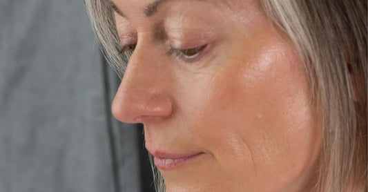 A mature woman with beautiful aging skin looks down with a gray background