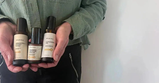 A closeup photo of Jewels Burdick, Founder of Simple Body holding three Simple Body Products including Brighten + Boost Tonic, Barrier Defense Serum and Cleansing Oil