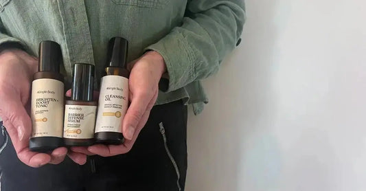 A closeup photo of Jewels Burdick, Founder of Simple Body holding three Simple Body Products including Brighten + Boost Tonic, Barrier Defense Serum and Cleansing Oil