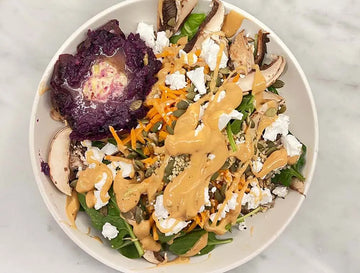 A photo of a delicious looking bowl of healthy food including mushrooms, cabbage, carrots, spinach, feta and a creamy dressing.