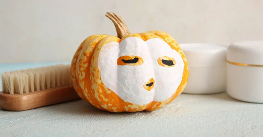 A photo of a pumpkin with a clay mask on it, a dry brush and Simple Body skincare products next to it.