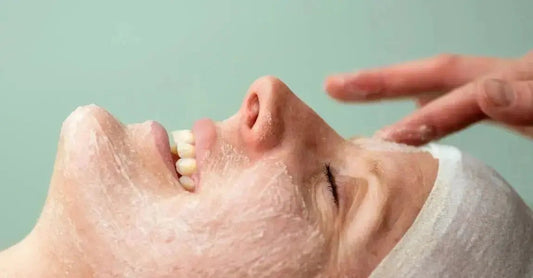 A photo of a young woman with Simple Body Bamboo Face Polish on her face, she's smiling and getting a facial massage.