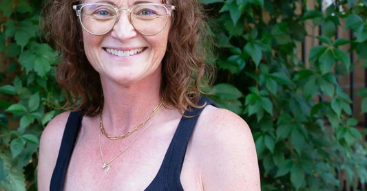 A photo of our founder, Jewels, looking into the camera and smiling with gold framed glasses and a black dress.