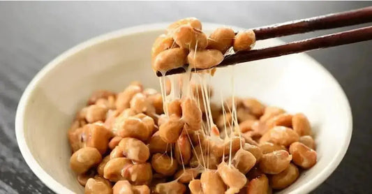 A bowl of fresh beans with string cheese stretching from the beans to the chopsticks.