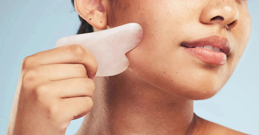 Person performing gua sha facial massage on the cheek using a rose quartz tool