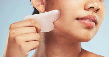 Person performing gua sha facial massage on the cheek using a rose quartz tool