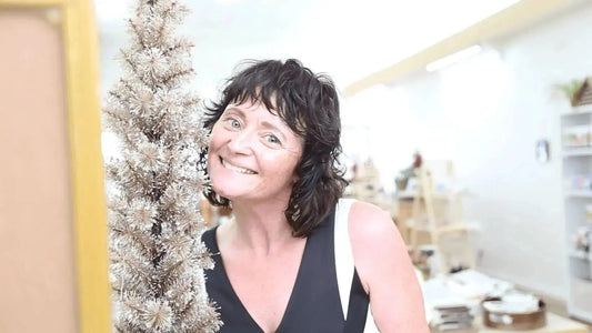 A photo of Simple Body Founder, Jewels smiling and standing next to a gold Christmas Tree.