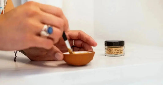 A closeup photo of a hand stirring a Simple Body Caramel Clay mask with a beautiful silver ring and blue stone.