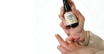 A photo of a hand holding a bottle of Simple Body Barrier Defense Serum. There's a drop of the Barrier Defense Serum on her fingertip showing off the creamy white texture.