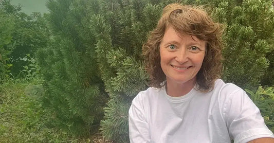 A photo of Jewels, Founder of Simple Body sitting in a field with greenery behind her.