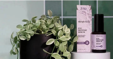 A photo of Simple Body Eye Defense Serum sitting on top of a white block with a green tile background and a healthy green plant next to it.