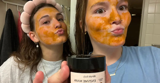 Two young girls with orange colored Simple Body Pumpkin Enzyme Masks on their faces pose for the camera.