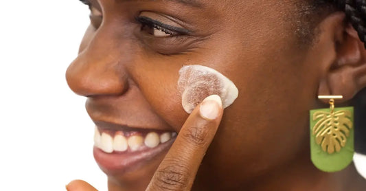 A photo of a young woman applying Simple Body Face Cream to her cheek smiling big.