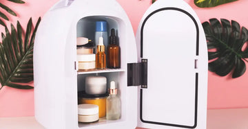 A photo of a mini fridge with skincare products inside with a pink background and natural leaves