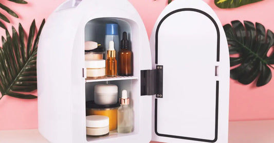 A photo of a mini fridge with skincare products inside with a pink background and natural leaves