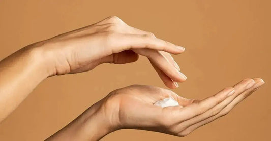 A photo of two female hands, one over the other getting ready to dip into a creamy lotion