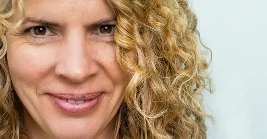 A closeup photo of Judy, a Simple Body customer, looking directly into the camer and smiling with gorgeous skin and beautiful curly blond hair.