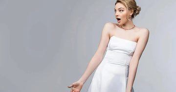Woman in a white strapless dress looks in shock and awe that her keratosis pelaris (chicken skin) is solved by Simple Body Bamboo Face Polish and Body Butter on a gray background.