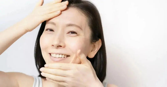 An asian woman smiles as she places on hand on her chin area and one hand on her forehead.