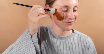 A young woman applying a Simple Body Caramel Clay Mask in a gray lounge soft sweatshirt.