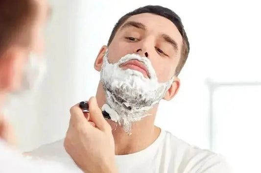 A photo of a young man looking in the mirror with shaving cream on his face shaving