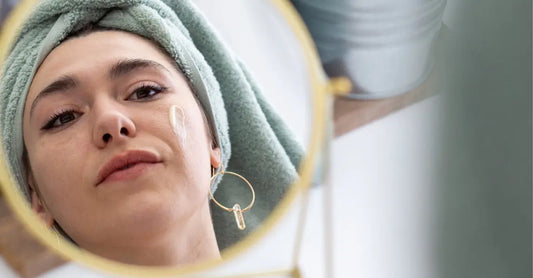 A photo of a beautiful women looking seriously in the mirror with a swipe of Simple Body Face Cream on her cheek with her hair wrapped up in a green towel