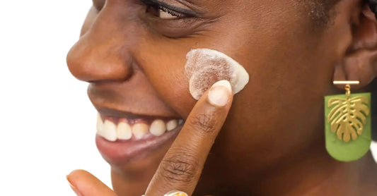 A very close up photo of a young women applying Simple Body Bamboo Face Polish to her skin with a smile on her face wearing a green and gold earring.