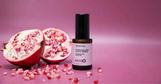 A photo of a pomegranate cut in half with seeds spilling out and a bottle of Simple Body Pomegranate Facial Serum sitting next to it.